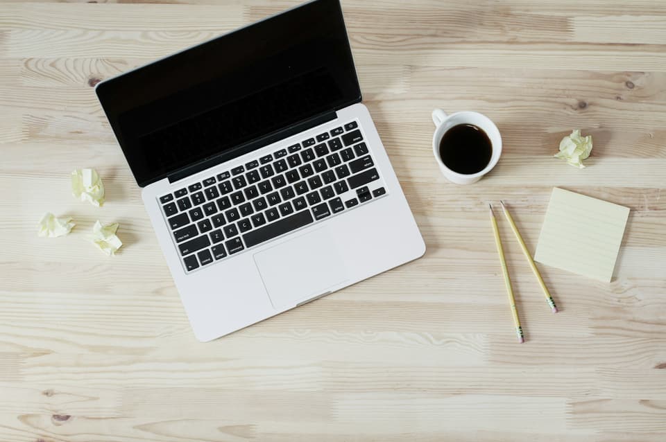 A laptop, a coffee and crumpled notes on a wooden desk